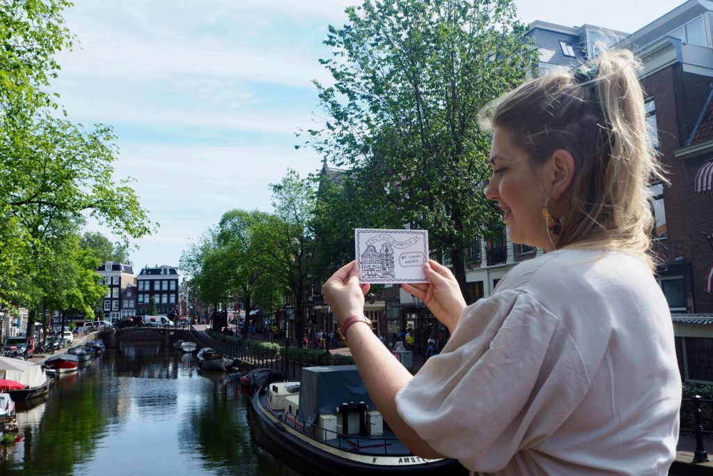 Tea holding one of the colouring postcards at a bridge in Amsterdam