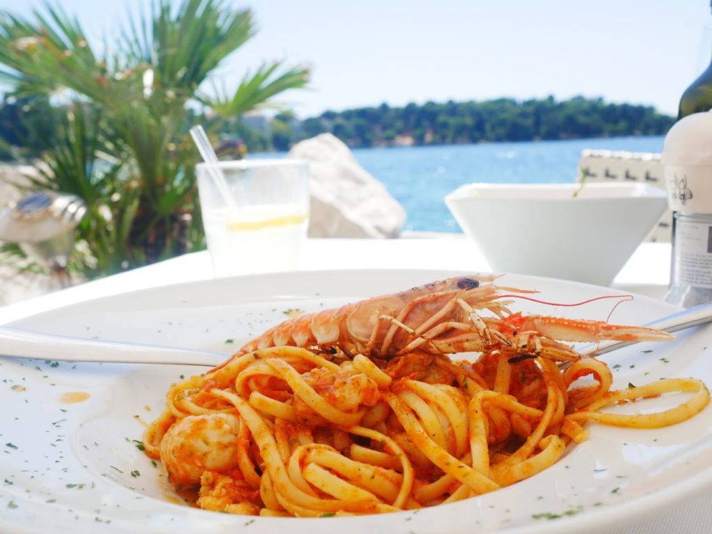 A plate with a seafood pasta on it and a sea in the background