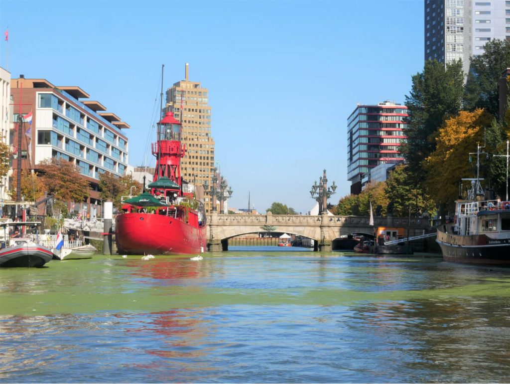 Red boat on one of the canals in Rotterdam with buildings on its shores