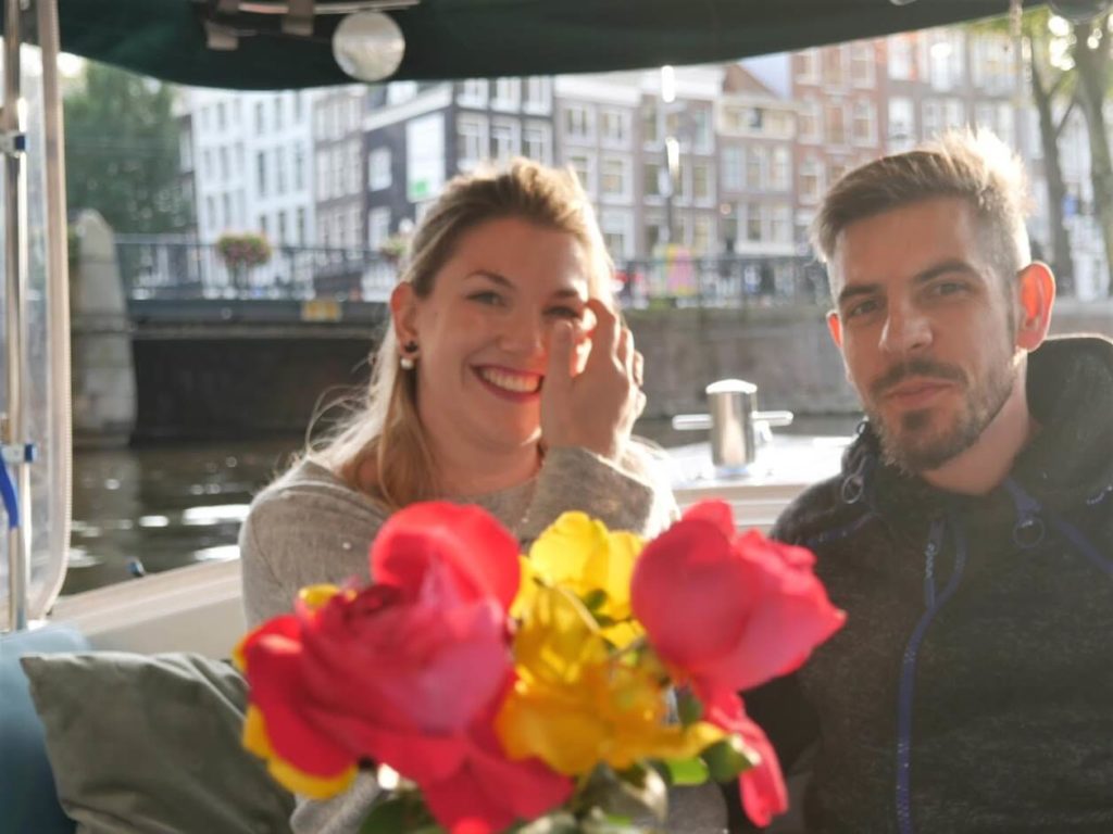 Couple on a small boat with flowers in a front, and Amsterdam in a back