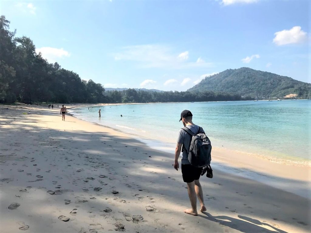 A man walking on a sandy beach next to the transparent blue sea